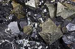 Magnetite exposed on the ground. The mineral is black and irregularly smooth. Individual chunks jut at angles characteristic of the crystal habit.