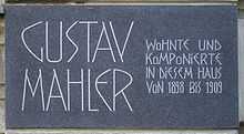  A dark plaque with white lettering in which the composer's name is shown in extra large characters on the left, the main message in smaller characters on the right