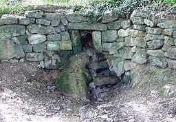 a very small stream issuing from an opening in a stone wall.