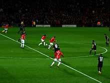 A wide shot of a football match with Manchester United in red in possession against Lyon in black.