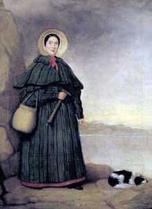 Portrait of a woman in bonnet and long dress holding rock hammer, pointing at fossil next to spaniel dog lying on ground.