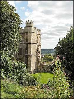 A stone tower connected to a ruined stone wall set among some trees