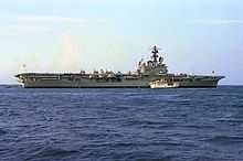 Colour photograph of a grey-painted aircraft carrier at sea. Several white aircraft are parked on its flight deck.