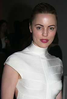 A photo of Melissa George, with her hair tied back, smiling, and wearing a white dress.