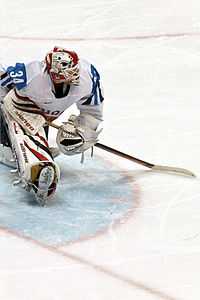 a goaltender in a blue and white uniform looks to his left as he stretches his legs