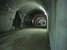 A long view down a lit gravel—paved concrete tunnel which has a series of openings on the left hand side