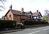 A brick and sandstone house near a road, with two gables and a dormer window, all timber framed.