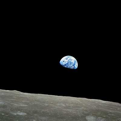 The small blue-white semicircle of Earth, almost glowing with colour in the blackness of space, rising over the limb of the desolate, cratered surface of the Moon.