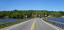 A road crossing a lake via a causeway. A sign is visible on the right-hand side of the road depicting the 311 designation. A car is visible in the distance.