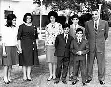 A group of related people posing outdoors. From left to right, there are three women dressed in shirts and long skirts, three boys dressed in suits and ties and a man in a suit and tie