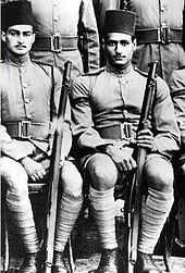 Two seated men in military uniform and wearing fez hats