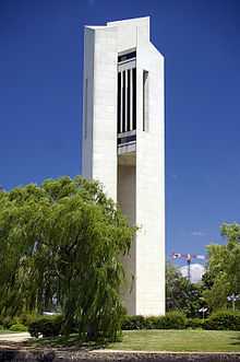 A tall modern concrete structure of three slabs, with the bells ensconced in the middle at the top, surrounded by landscaped grass and hedge.