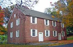 A brick house with white shutters seen from underneath a tree branch. The trees on either side are showing autumn color