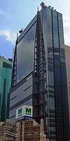 Ground-level view of a blue, glass, rectangular high-rise; attached to one side of the building are two structures consisting of poles that run the height of the building