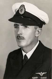 Head-and-shoulders portrait of man with moustache wearing dark-coloured jacket with black-and-white peaked cap}