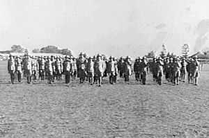 Rows of men in light-coloured military uniforms and pith helmets in a field