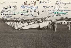 Side view of biplanes in a row at a field, along with some men in light-coloured military uniforms and pith helmets