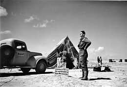 Man in flying suit standing outside tent marked "450 OPS"; two other men near tent and truck marked "RAAF" to the side