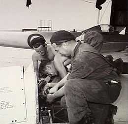 Three men in overalls working on an aircraft engine