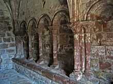 A blind arcade seen from an angle showing four round-headed arches supported on columns with carved capitals; a bench runs along the base