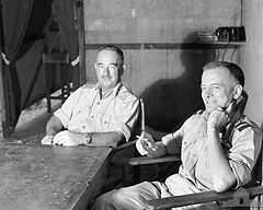 Two men in light-coloured uniforms seated at a table