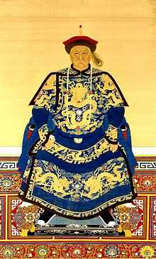 Full-face painted portrait of a severe-looking sitting man wearing a black-and-red round cap adorned with a peacock feather and dressed in dark blue robes decorated with four-clawed golden dragons