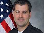 Portrait photo of Michael Slager in police uniform with an American flag partially visible in the background.