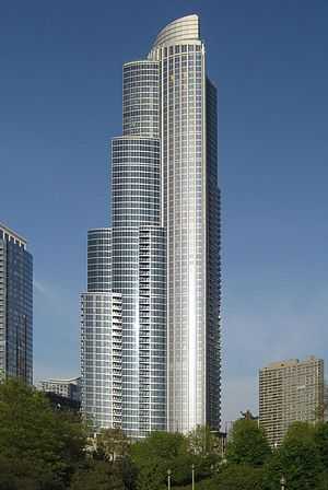 tall silver skyscraper with blue sky background beyond tall trees