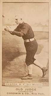 A man in a baseball uniform has his arm out in front of body attempting to catch a baseball.