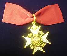 Photograph from above of a badge of a Companion of the Order of the Bath lying on a navy blue fabric.