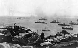 A group of large warships steaming slowly off a city.