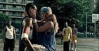  An African American man holding a young blonde woman in her arms. They are standing in a basketball court. The woman is putting her hands into the man's face.