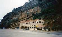 Two story stone structure built into the side of a cliff. The second floor has an outdoor balcony.