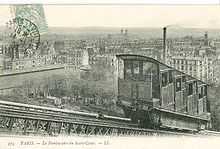 A sepia postcard taken at an angle to the track showing one of the first funicular's cabins. Its stepped compartments are clearly shown. In the background is a panorama of Paris