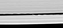 Two bright bands run from the left to right. In the narrow gap between them (Keeler gap), which has wavy edges, a small oblong object can be seen.