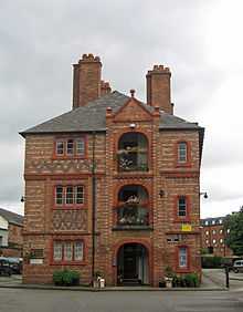 The end of a block of three-storey flats with an arched area on each floor, terracotta dressings and brick diapering.