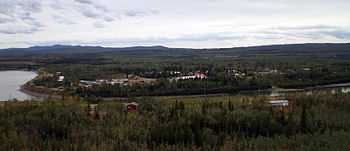 A collection of houses and buildings surrounded by trees and a river are seen.