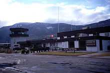 The main terminal building of an airport, with a "Penticton" sign near the entrance, as well as a "Arrivals" sign pointing to the right, with the same word written in French below it.