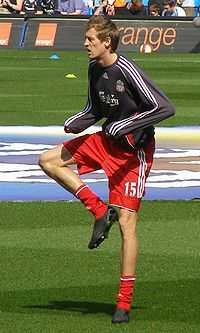 A man in a football uniform, standing on one leg, warming up before a football match