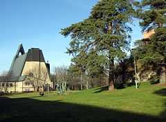 A southern view of the rear entrance to the church. In the foreground is playground equipment, a grass lawn and some trees.