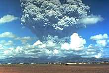 A tower of grey ash erupts above a mountain