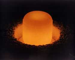 Glowing cylinder of plutonium oxide standing in a circular pit