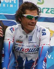 A road racing cyclist in a white and blue jersey with red trim, wearing sunglasses with white frames.