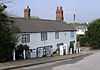 A long cottage in two storeys with tall chimneys and windows with intricate white-painted tracery.