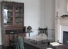 Photography of a library, showing a hutch with books in it and a table with various items on it.