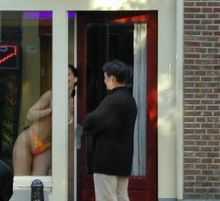 A photograph depicting a woman wearing an orange bikini leaning out of an open doorway in front of a man wearing a black jacket