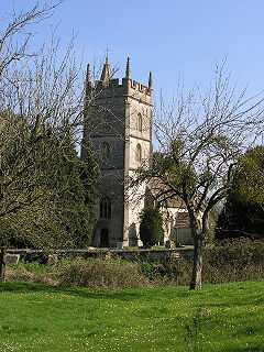 Stone building with prominent square tower. Surrounded by trees and with green grass area in the foreground separated from the building by a stone wall.