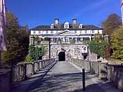 At the end of a bridge over a moat, a grand castle surrounded by trees