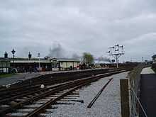 Curving concrete station platform. There is a small wooden hut on the platform.