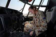 A woman wearing a camouflaged military uniform sitting in the cockpit of an aircraft